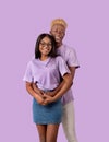 Cheerful African American guy hugging his beloved woman from behind, smiling and looking at camera on lilac background