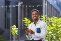 Cheerful african american guy using mobile phone sitting on bench in city park outdoors. Happy black man in casual clothes with a Royalty Free Stock Photo