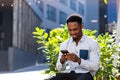 Cheerful african american guy using mobile phone sitting on bench in city park outdoors. Happy black man in casual clothes with a Royalty Free Stock Photo