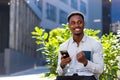 Cheerful african american guy using mobile phone sitting on bench in city park outdoors. Happy black man in casual clothes with a Royalty Free Stock Photo