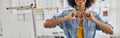 Cheerful African-American lady tailor shows heart with hands standing by modern sewing machine