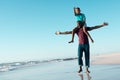 Cheerful african american man with arms outstretched carrying son on shoulders at seashore under sky