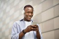 Happy African American man in headphones picking music playlist on smartphone near brick wall outside