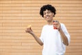 Cheerful African-American man holding a cup of coffee and an orange donut Royalty Free Stock Photo