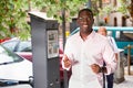 Cheerful African American man showing ticket for car parking purchased in parking meter on city street Royalty Free Stock Photo