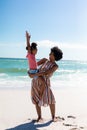 Cheerful african american mother carrying daughter while enjoying sunny day at beach against sky Royalty Free Stock Photo