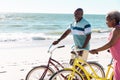 Cheerful african american senior couple with bicycles enjoying at beach against seascape and sky Royalty Free Stock Photo