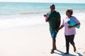 Cheerful african american senior couple with mats holding hands while walking at beach on sunny day Royalty Free Stock Photo