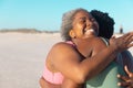 Cheerful african american senior mother embracing young daughter while enjoying at beach against sky Royalty Free Stock Photo