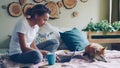 Cheerful African American student is using laptop doing homework sitting on bed at home while her adorable pet dog is Royalty Free Stock Photo