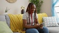 Cheerful african american woman with braids enjoying home comforts, sitting on sofa and having fun texting online using her Royalty Free Stock Photo