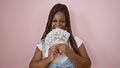 Cheerful african american woman with braids exuding confidence, posing over a pink isolated background, smiling while holding a Royalty Free Stock Photo