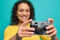 Cheerful African American woman photographer in bright yellow clothes smiling toothy smile while holding an old retro style Royalty Free Stock Photo