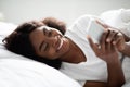 Cheerful african american woman using cellphone in bed Royalty Free Stock Photo