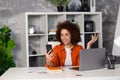 Cheerful african american young businesswoman laughing while talking on video call over mobile phone in office with laptop Royalty Free Stock Photo