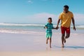 Cheerful african american young man and son holding hands while running at beach against blue sky Royalty Free Stock Photo