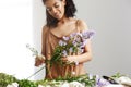 Cheerful african female florist smiling working holding branch of daisy over white wall. Royalty Free Stock Photo