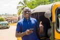 cheerful african man standing next to his tuk tuk taxi smiling and using his smart phone giving a thumbs up Royalty Free Stock Photo