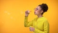 Cheerful Afro-American female blowing soap bubbles, having fun, childhood game