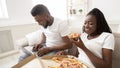 Cheerful afro couple spending weekend with pizza and laptop