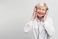 Cheerful aged woman listening to music in headphones. She is enjoying the moment. on white background.