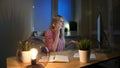 Happy female at computer talking on smartphone. Cheerful amazed blond woman in checkered shirt sitting at night at Royalty Free Stock Photo