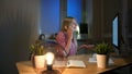 Happy female at computer talking on smartphone. Cheerful amazed blond woman in checkered shirt sitting at night at Royalty Free Stock Photo