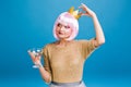 Cheerful amazing young woman with pink haircut having fun on blue background. Golden crown on head, brightful makeup Royalty Free Stock Photo