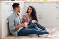 Cheerful Arab Couple Drinking Coffee In Kitchen, Sitting With Cups On Floor