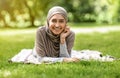 Cheerful arab girl in hijab lying on grass at park