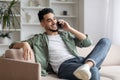 Cheerful arab guy having phone call while relaxing on couch at home Royalty Free Stock Photo