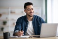 Cheerful arab guy working on laptop, taking notes Royalty Free Stock Photo