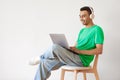 Cheerful arab man working on laptop and wearing headphones, sitting on chair over light studio wall, copy space Royalty Free Stock Photo
