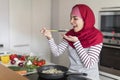 Cheerful arab woman housewife cooking on electric stove, tasting food Royalty Free Stock Photo