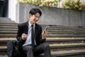 A cheerful Asian businessman is showing his fist and looking at his phone with a happy face Royalty Free Stock Photo