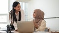 Cheerful Asian businesswoman and her muslim colleague are enjoying sharing their ideas for a project Royalty Free Stock Photo