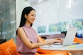 Cheerful Asian businesswoman working on laptop at corporate workplace. Happy and successful white collar professional