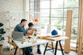 Cheerful Asian carpentry father discusses and teaches his son about construction instruments on the table at the home workshop Royalty Free Stock Photo