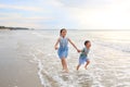 Cheerful Asian child girl and little boy having fun run together and hand in hands on tropical sand beach at sunset. Happy family Royalty Free Stock Photo