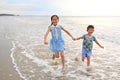 Cheerful Asian child girl and little boy having fun run together and hand in hands on tropical sand beach at sunset. Happy family Royalty Free Stock Photo