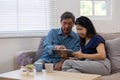 Cheerful Asian couple using network video call tablet sitting together on sofa at home Asian elderly husband sitting Royalty Free Stock Photo