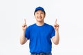 Cheerful asian delivery guy with braces, wearing blue uniform, pointing and looking at top advertisement, demontrate