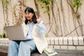 Cheerful asian girl making video call on laptop while sitting outdoors on the bench Royalty Free Stock Photo