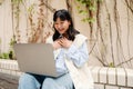 Cheerful asian girl making video call on laptop while sitting outdoors Royalty Free Stock Photo