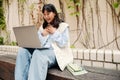 Cheerful asian girl making video call on laptop while sitting outdoors Royalty Free Stock Photo