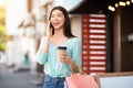 Cheerful asian girl with shopping bags and coffee talking on cellphone outdoors Royalty Free Stock Photo