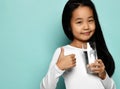 Cheerful asian girl in white longsleeve standing with glass of pure water and showing thumbs up sign