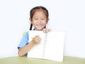 Cheerful Asian little child girl in school uniform show writing on blank notebook sitting at desk isolated over white background Royalty Free Stock Photo