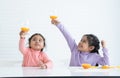 Cheerful Asian little children girls holding, drinking fresh orange juice from glass and raising glass up after making orange Royalty Free Stock Photo