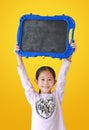 Cheerful asian little girl holding blank black board isolated on yellow background. Kid show empty blackboard Royalty Free Stock Photo